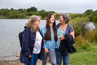 Two ladies and teenage girl laughing outdoors beside a lake