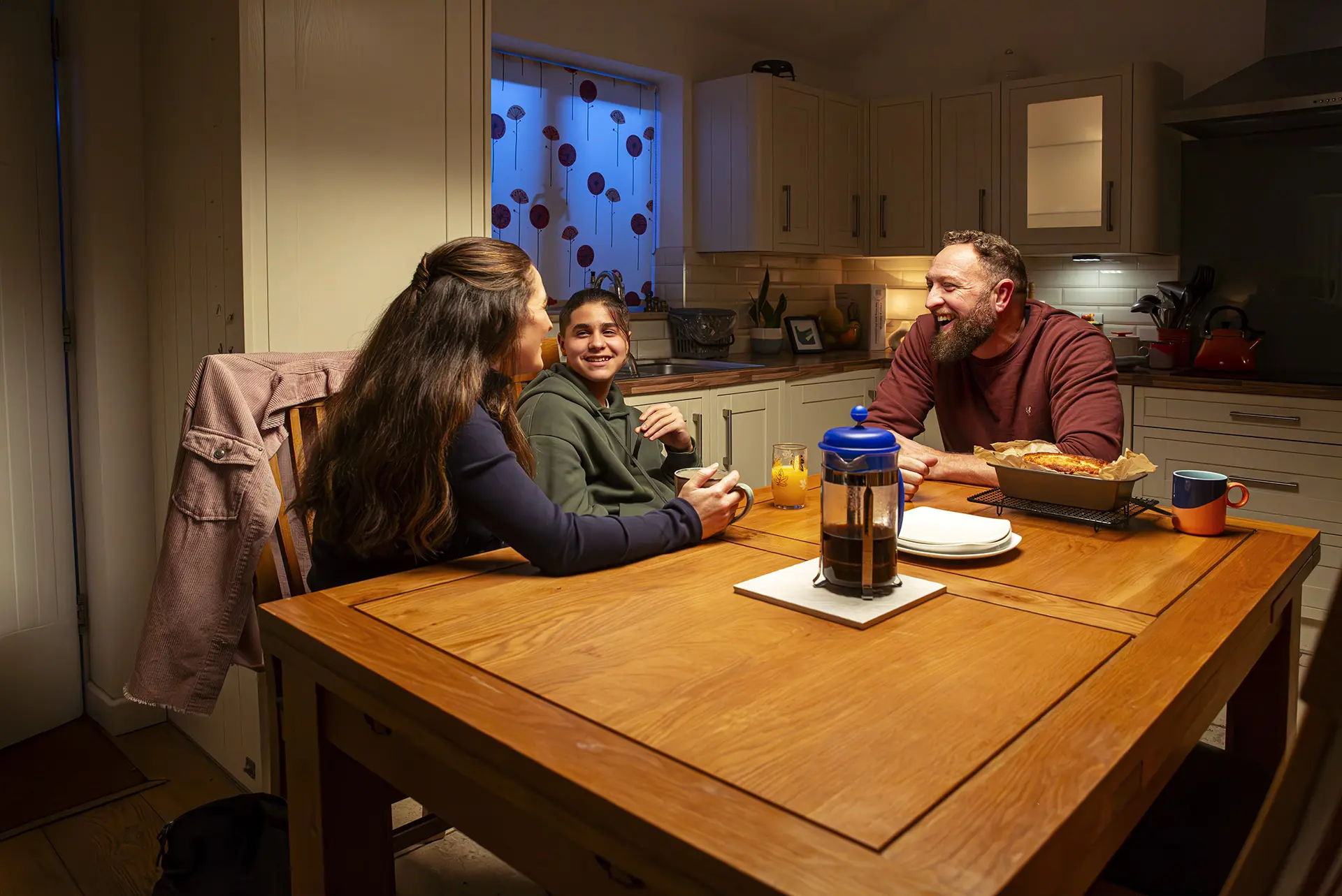 Female social worker, teenage boy and man sat at a kitchen table