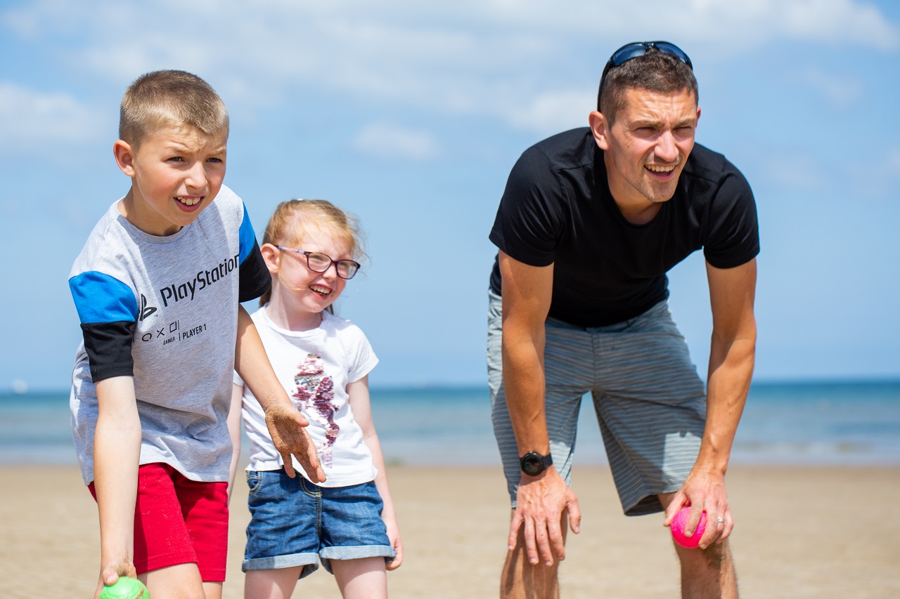 Man wearing black tshirt playing bowls on the beach with children