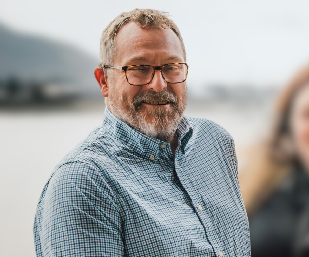 Mel panther, man with beard and glasses standing smiling wearing a blue check shirt.